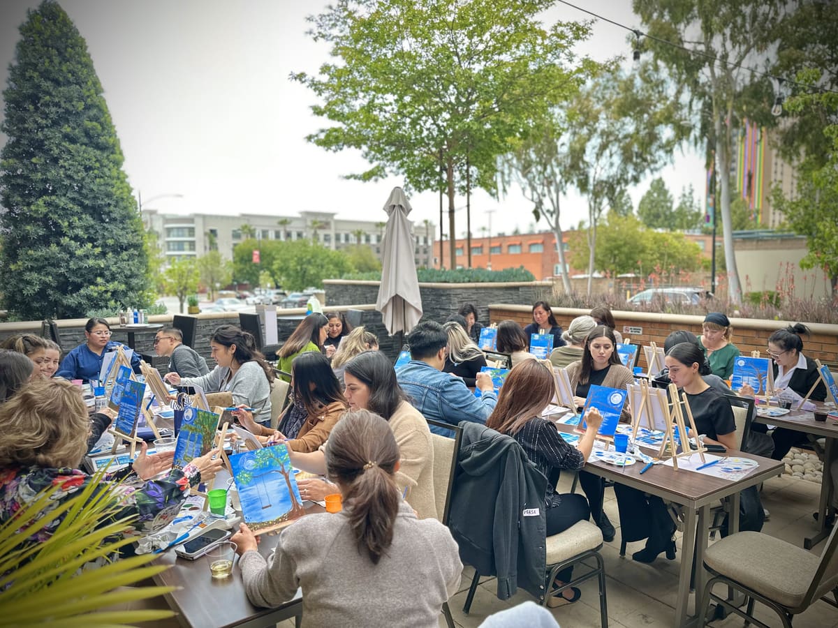 A company team painting together at long tables in an outdoor courtyard