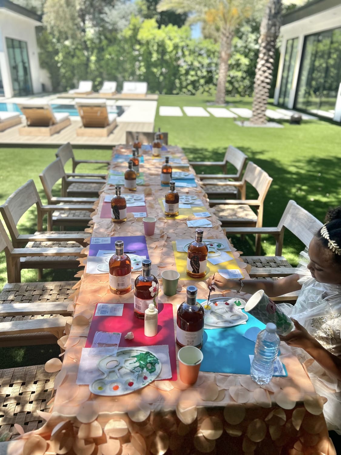 A long outdoor table styled with colourful placemats and palettes beside the pool